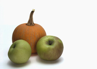 An orange pumpkin and two green apples to left of frame on a white background.  There is ample room for text.  The fresh produce is representative of fall harvest or autumn.