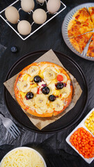 Fresh homemade Italian pizza with banana toppings and baking ingredients on rustic wooden table