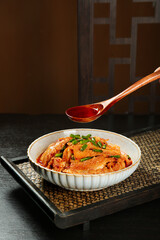 Spicy Red Tripe Stew in Bowl with Sauce Being Poured from Wooden Spoon