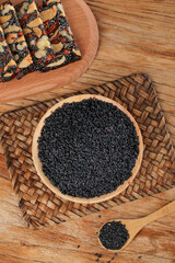 Black Sesame Seeds and Cooked Sesame Brittle in Wooden Bowls on Rustic Wood Background