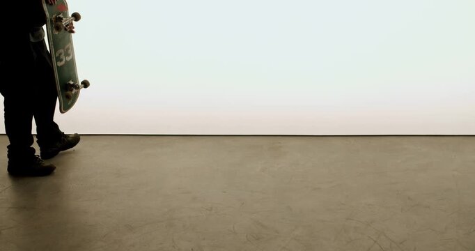A young skater picks up their skateboard in a minimal studio setting. The bright background and simple environment create a clean look. This is great footage for extreme sports, skateboarding culture,