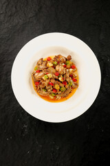 Spicy Chinese Beef and Chicken Stir-Fry with Fresh Vegetables and Peppers on Dark Stone Background