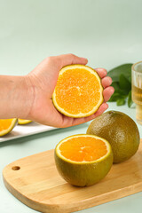 Fresh Orange Slice in Hand with Cut Citrus Fruits on Wooden Cutting Board