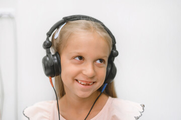 Smiling child wearing headphones for an audiometry test. Pediatric hearing examination in a medical...