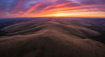 Naklejka premium Dramatic sunset over rolling hills creates a vibrant landscape panorama