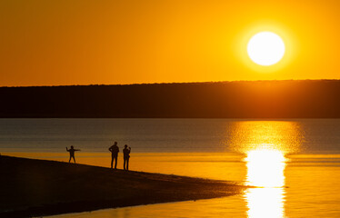 Family watching a romantic sunset with child playing around, Monkey Mia, Shark Bay, Western Australia