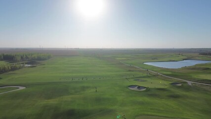 Aerial drone footage flying in a perfectly straight line over a long, symmetrical golf course fairway, with the bright sun shining directly ahead, creating a beautiful, bright atmosphere.
