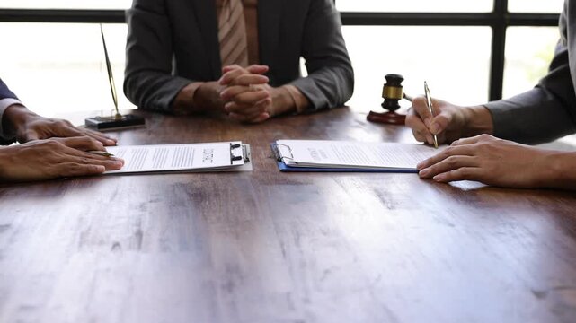 Lawyers mediating and signing a contract after a successful negotiation, reaching a compromise on a wooden table with a gavel.