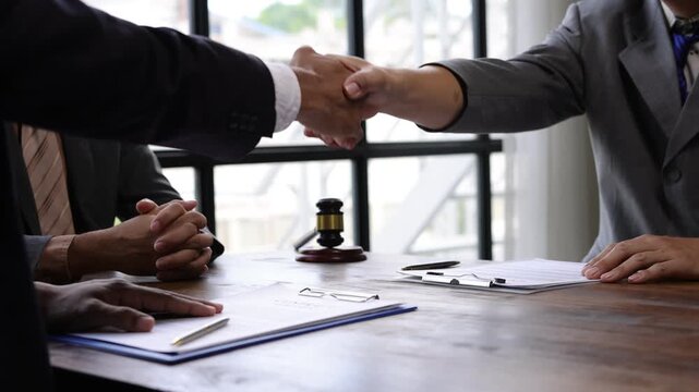 Professional lawyers sealing successful partnership through firm handshake after signing legal contract in corporate office, representing collaborative business agreement.
