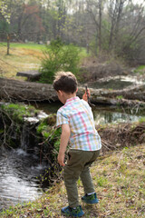 little boy in the woods throwing stick into creek