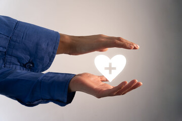 Heart with a health sign in the middle held between a pair of hands