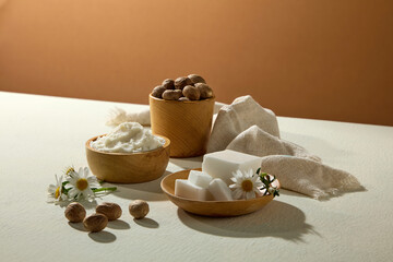 Still life of shea butter, chamomile blossoms, and nuts on brown background with soft shadows. A warm tone setup for skincare branding.