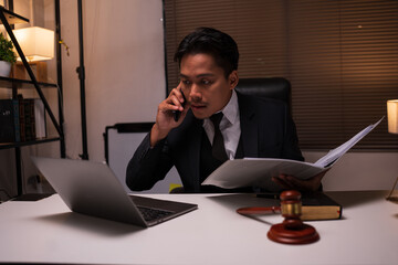 A focused male lawyer in a formal suit sits at his desk, diligently reading a thick law book. In...