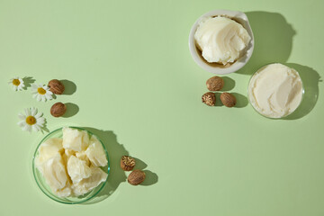 Flat lay with creamy shea butter, raw nuts and chamomile flowers on pastel green background, styled for cosmetic and spa promotional design.
