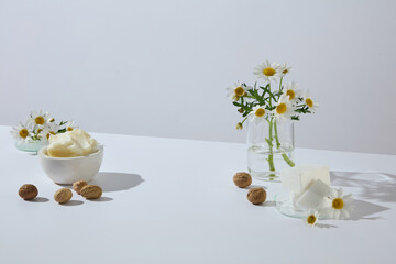 Natural display of shea butter, shea nuts, and fresh chamomile flowers on a white background, ideal for advertising skincare and cosmetic product designs. Blank space for product display
