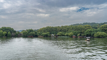 Chinese tourist boats with awnings, canopies, and lifebuoys float on the picturesque lake. Lush green vegetation on the shores. Blue sky, clouds. China. Hangzhou. West Lake Xi Hu