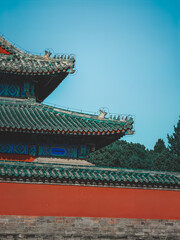Vibrant blue sky over a majestic traditional East Asian building with intricate green tiled roofs and a striking red wall.