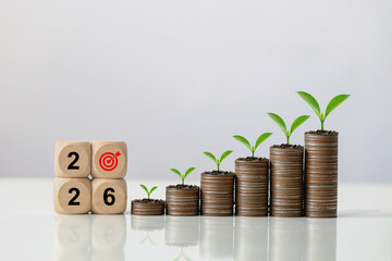 2026 wooden blocks with a target icon beside ascending stacks of coins topped with green seedlings with copy space, representing financial planning, investment strategy, and New Year economic growth.