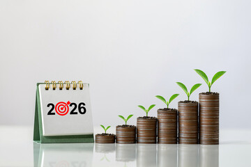 2026 desk calendar next to ascending stacks of coins with green seedlings on a white background, symbolizing financial planning, investment strategy, economic growth, and New Year wealth building.