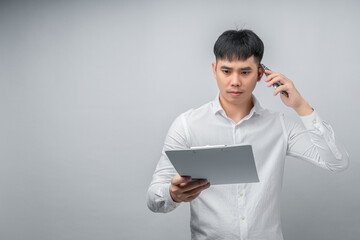 A handsome Asian young man expresses shock and sadness while reviewing a financial document and using a smartphone for checking. Concept for business, finance, technology and lifestyle themes.