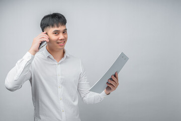 A handsome Asian young man smiling happily while reviewing a financial document and using a smartphone for checking information. Concept for business, finance, technology and lifestyle themes.