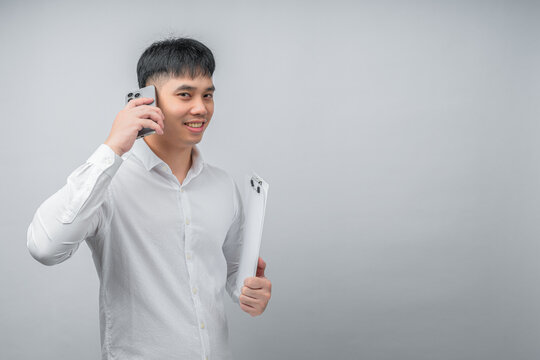 A handsome Asian young man smiling happily while reviewing a financial document and using a smartphone for checking information. Concept for business, finance, technology and lifestyle themes.