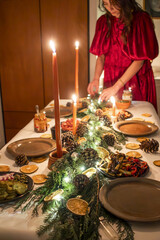 Woman in Red Dress Setting Festive Christmas Dinner Table with Garland
