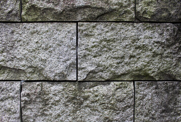Close up of square stone wall texture. Rough surface of stacked stones background. Trash stuck in gaps between stones.