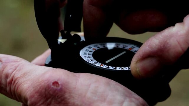 Closeup of hand holding a compass looking for direction. Compass reading and land navigation concept. Tourist compass and magnetic declination calculator. Navigation, searching, exploring concept.