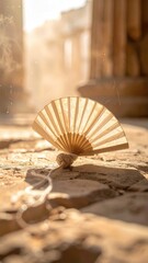 Open fan rests on stone in sunlight among aged columns