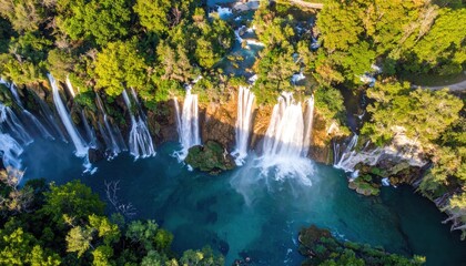 Majestic aerial view showcases a vibrant waterfall cascading down rocky terrain into a turquoise river surrounded by lush green trees, creating a serene and scenic natural environment under bright...