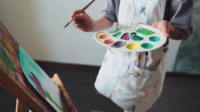 Child creating colorful artwork with paint and brush. Imaginative girl practices creativity and grows artistic skill in peaceful home studio. Great image for education and art topics