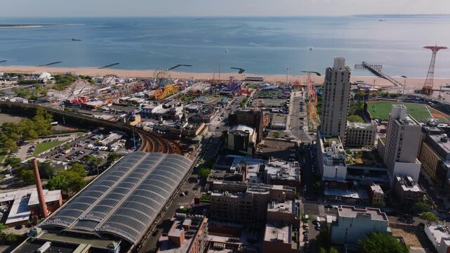 Aerial view of Coney Island Stillwell Avenue subway terminal, residential and commercial buildings, and surrounding city streets with Kaiser Park visible in the distance.