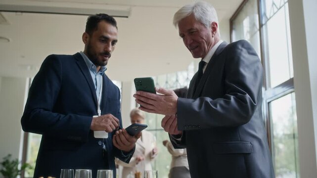 Low angle view of two diverse businessmen holding smartphones sharing their contacts during business event