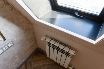 A corner view shows a modern window with a dark sill, a white radiator below, textured walls, and...