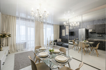 Bright apartment interior featuring a dining area with a glass table, beige chairs, and a...