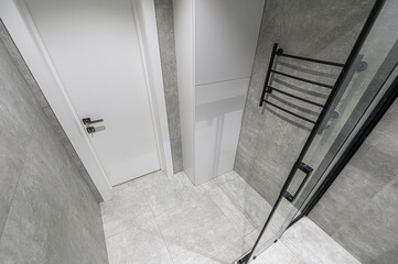 A modern bathroom showcases gray tile, a white door and cabinet, and a black towel rack and shower enclosure. Clean and minimalist design