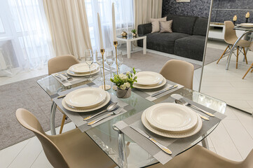 A well-lit dining area featuring a glass table set for four, complete with elegant white plates, silverware, candles, and champagne flutes
