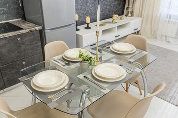 An inviting dining setup features a glass table adorned with place settings, complete with elegant plates and cutlery. Candles add a touch of warmth to the modern decor