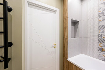 Modern bathroom entry: white geometric-patterned door with gold handle, black ladder radiator on...