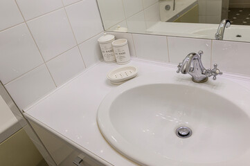 Classic bathroom vanity: white oval porcelain sink, ornate chrome bridge faucet, Les Bains Paris soap jar/mug, white soap dish, glossy white countertop, subway tiles, mirror reflecting tub