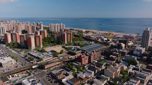 Aerial view of Coney Island Stillwell Avenue subway terminal, residential and commercial buildings, and surrounding city streets with Kaiser Park visible in the distance.