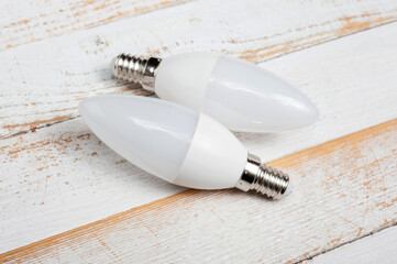 Two LED lamps with E14 sockets lying on a wooden surface.