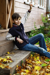 Smiling Boy in Autumn Backyard Scene with Raised Hand on Wooden Steps