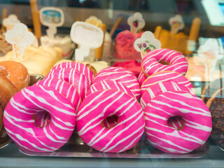 Juicy pink donuts on the store counter, food in the store, unhealthy and fatty food, sweets. Pink and white donuts on a display. There are many of them. They are arranged in a row