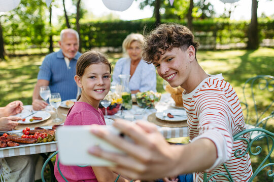 Family gathering for barbecue in summer garden, taking selfie. - Powered by Adobe