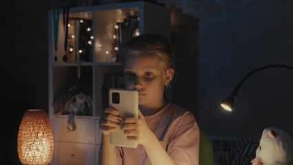Young girl using smartphone in cozy room at night with soft lighting and decorative items visible
