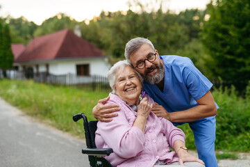 Male home nurse taking care of elderly woman in wheelchair.