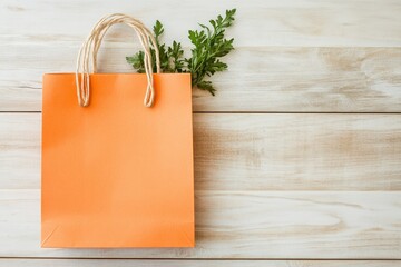 A vibrant orange paper shopping bag sits atop a light wood surface, accented by delicate greenery.
