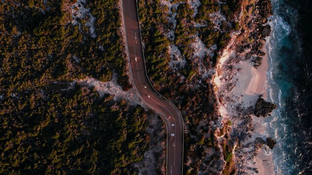 Winding coastal road with lush greenery and ocean waves at sunset in a serene environment - Powered by Adobe